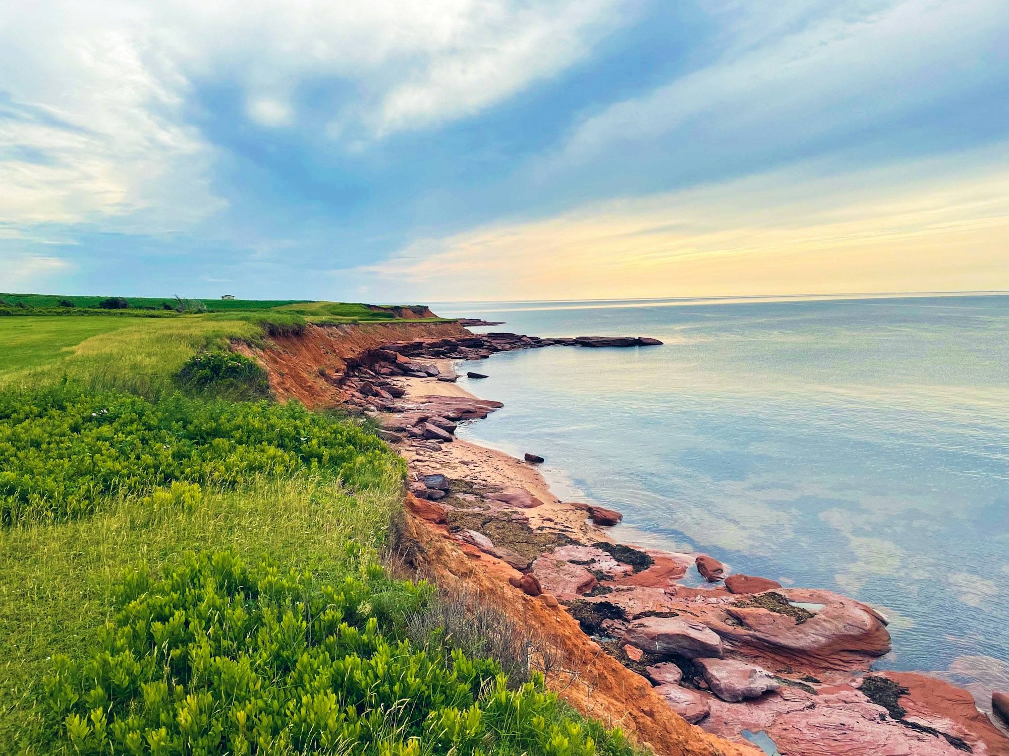 Red sandstone cliffs and a grassy headland above a calm sea at sunset, Prince Edward Island
